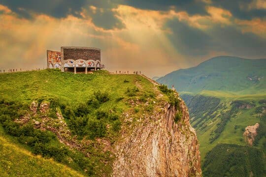 Abandoned Soviet bus perched on cliff edge overlooking green valley and mountains in Georgia